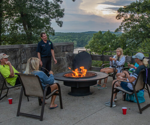 a family sits around a campfire on the patio of the mochican