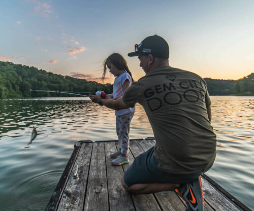 Father helps daughter hook a fish at the lake